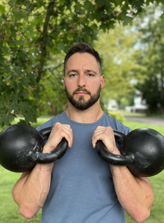 Image of a fitness instructor taking a self portrait outdoors while holding two kettlebells